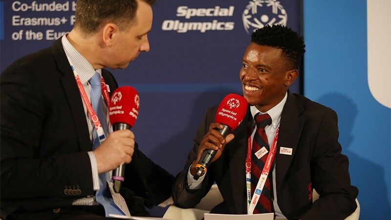 Two men speaking into microphones while sitting down facing each other.