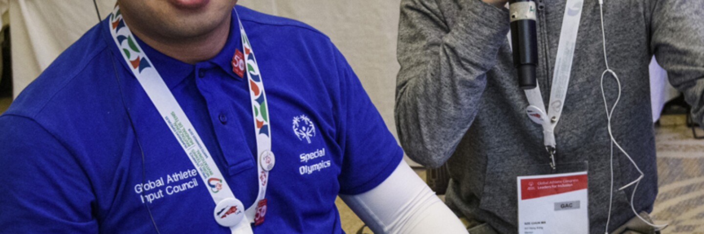 Athletes sitting at a table, one is talking. 