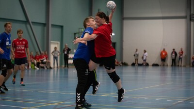 A woman wearing a red jersey jumping, holding a ball  colliding with a man on the opposing team, wearing a blue jersey