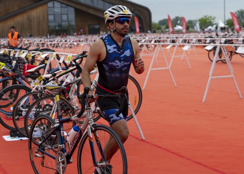 an athlete in a blue camouflage uniform and a bike helmet walks alongside his bicycle