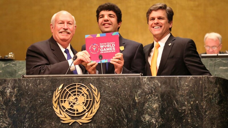 Bob Corlew, Dr. Timothy Shriver, and Special Olympics athlete Mina Baghat standing at a podium at the United Nations. 