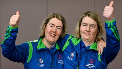 Twins wearing Special Olympics Ireland jackets smiling with their thumbs up