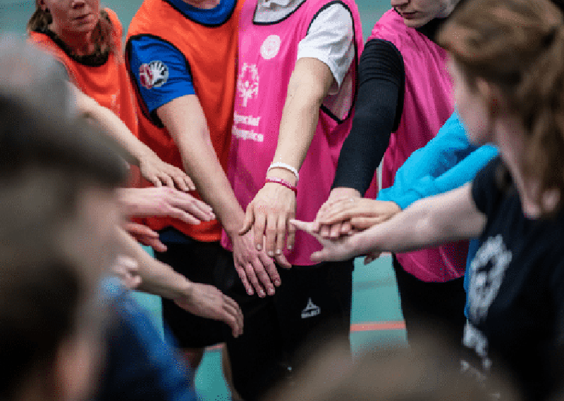 Group of people standing in a circle all putting their hands in the middle. 