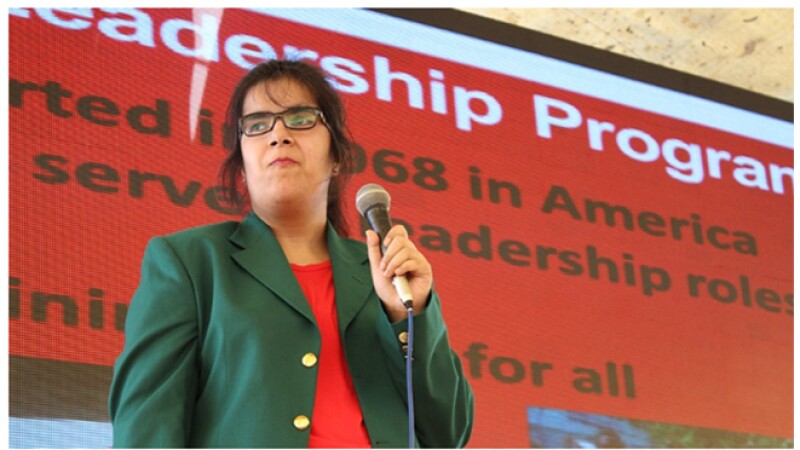 Woman holding microphone while speaking to group of people.