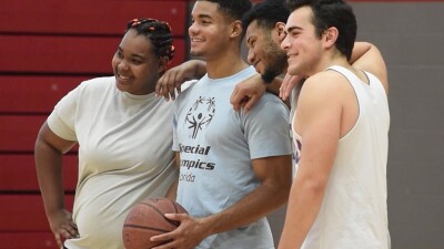 Group of four with their arms on one another shoulders; one is holding a basketball. 