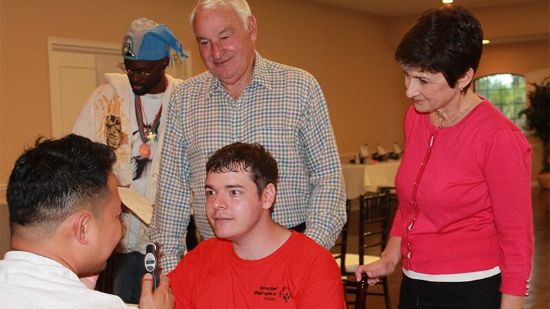 Ann Costello and Tom Golisano watch an athlete receive an eye exam. 