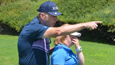 Amy standing in front of her father as he gives her advice on the green. 