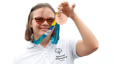 Woman wearing Special Olympics Italy shirt smiles and showcases bronze medal