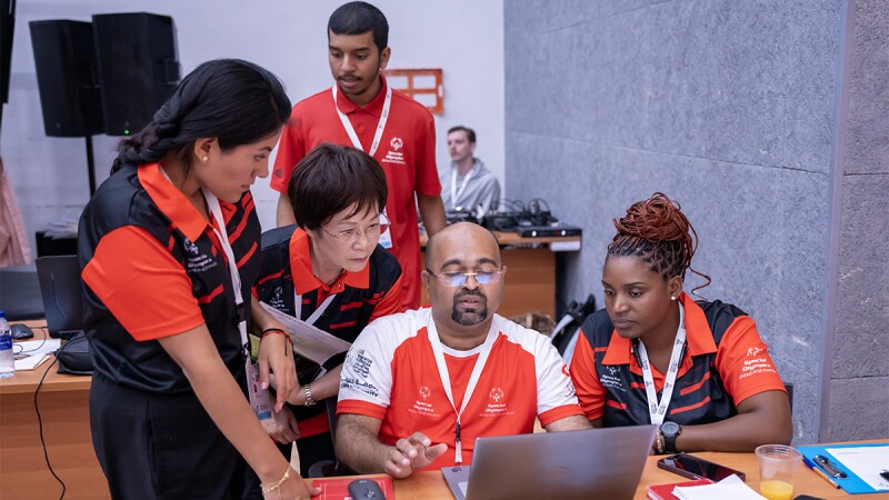 Four people watch as a man works on a laptop. 