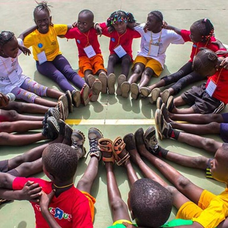 young athletes sitting in a circle with their feet together forming another circle. 