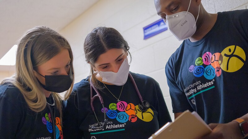 Three people wearing Healthy Athletes branded t-shirts and looking over a paper on a clipboard. 