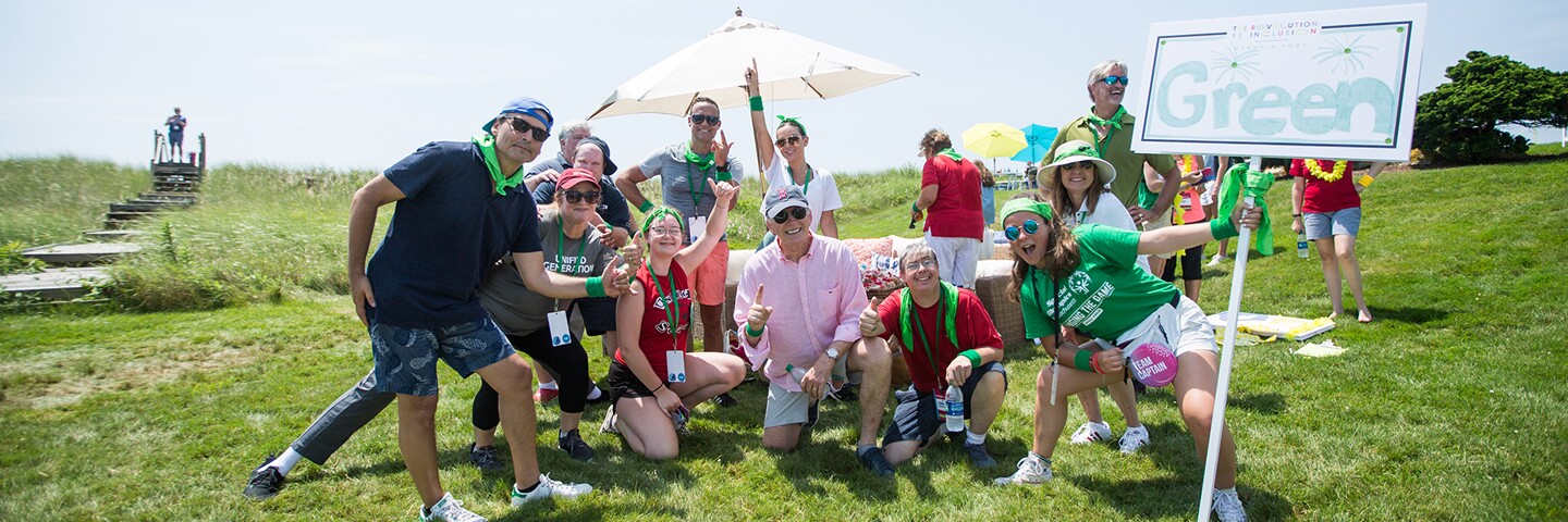 group of people outside on a grassy field standing close for a group picture. 