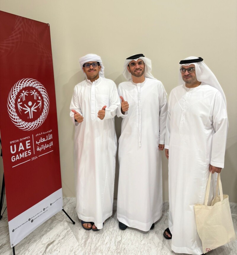 Three men standing next to Special Olympics UAE signage