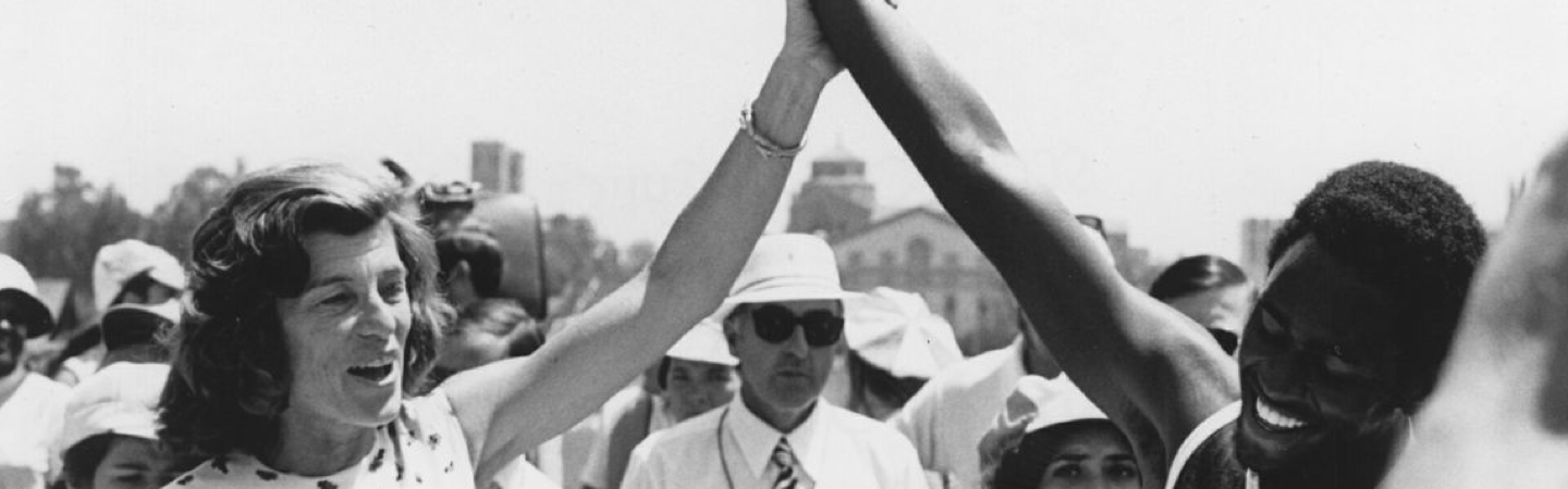 Black and white photo of a smiling Eunice Kennedy Shriver holding up the arm of a champion at the inaugural 1968 World Games in Chicago