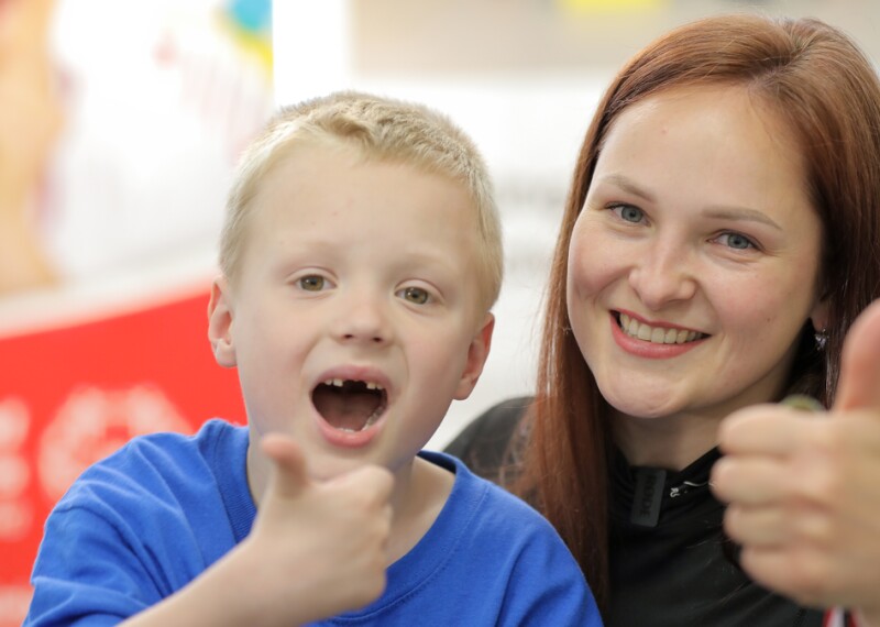 A blond boy and a woman smile with their thumbs up while posing for the photo