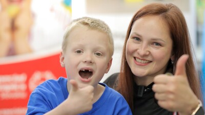 A blond boy and a woman smile with their thumbs up while posing for the photo