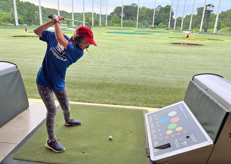 Woman hitting a ball at a topgolf course. 