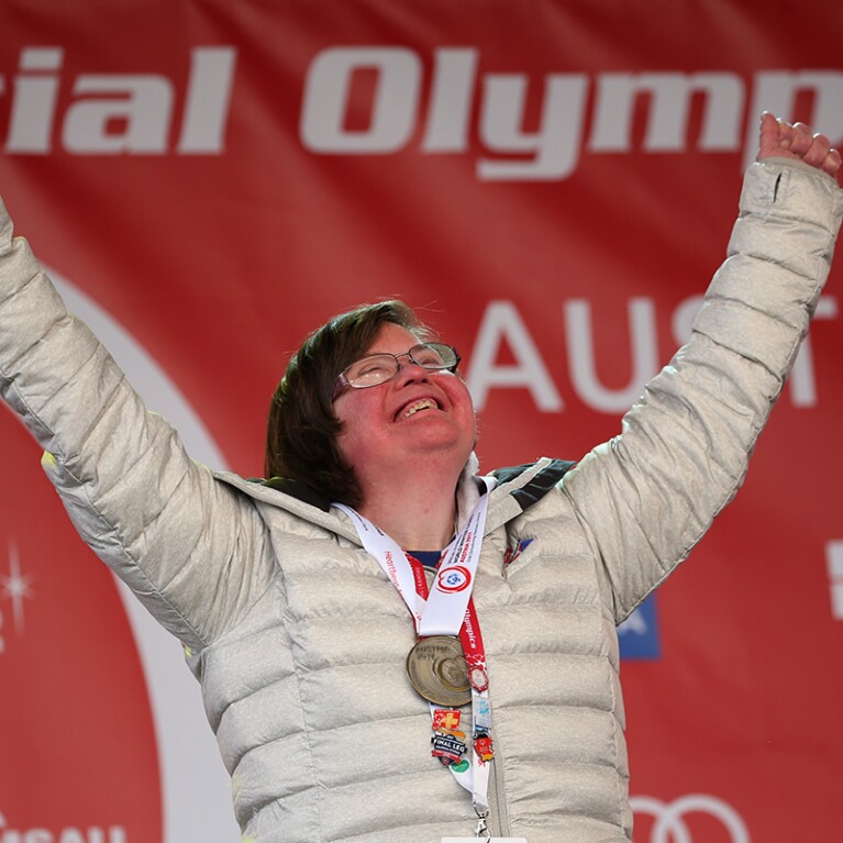 Athlete celebrating with her arms up and medal around her neck. 