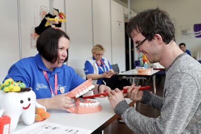 Volunteer helping athlete demonstrate the correct way to brush teeth. 