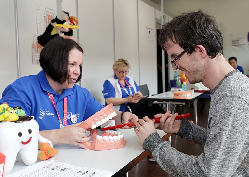 Volunteer helping athlete demonstrate the correct way to brush teeth. 