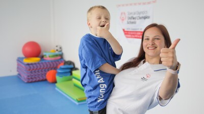 A woman holding a young boy, both smiling and giving a thumbs up