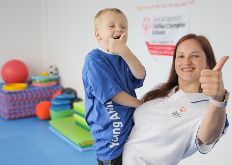 A woman holding a young boy, both smiling and giving a thumbs up