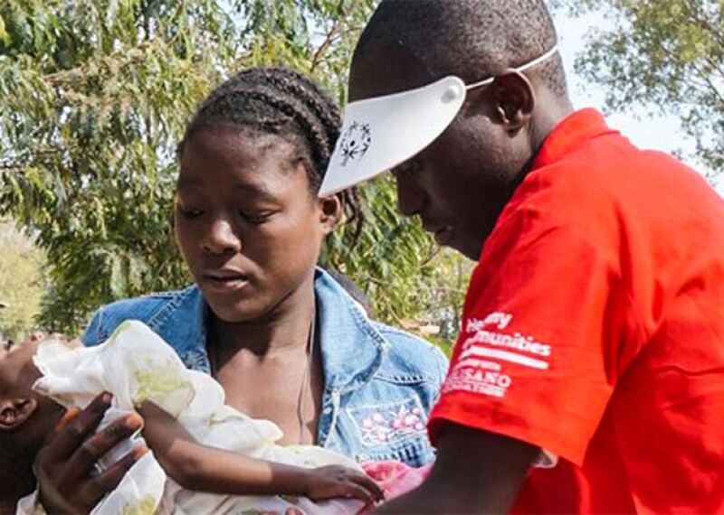 Man and woman standing outside. Woman is holding her baby and man in Special Olympics Golisano branded red short sleeve polo shirt and white Special Olympics branded visor is looking at her baby.