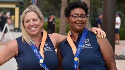 Two women standing side by side with their arms around one another shoulders. 