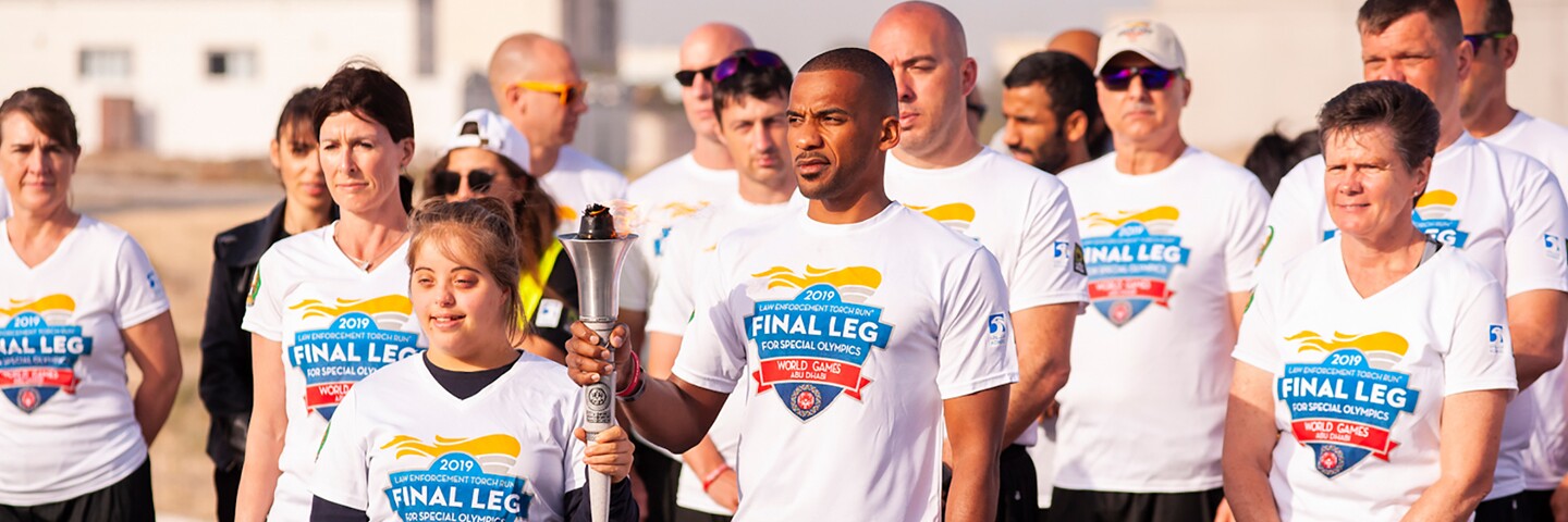 Runners standing together in a group, the two lead runners are holding the Torch of Hope together. 