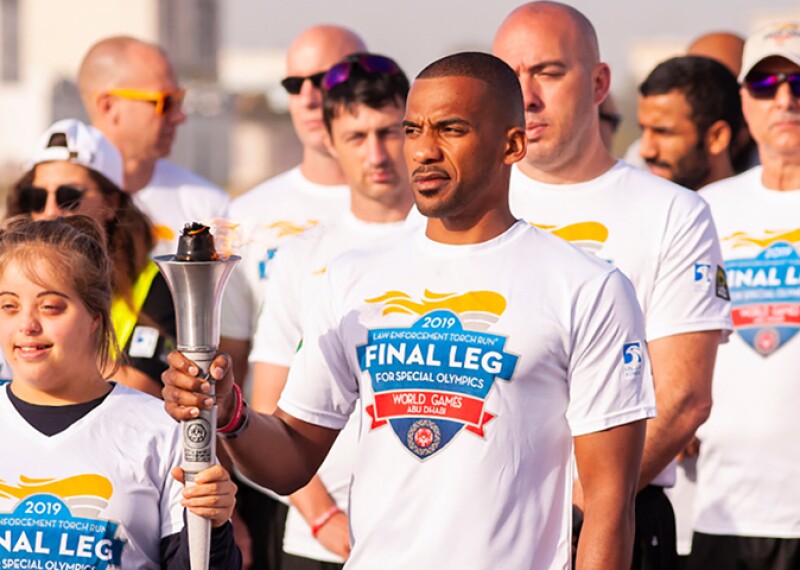 Runners standing together in a group, the two lead runners are holding the Torch of Hope together. 