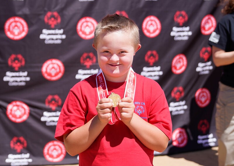 Young male athlete holding up his goal medal and smiling. 